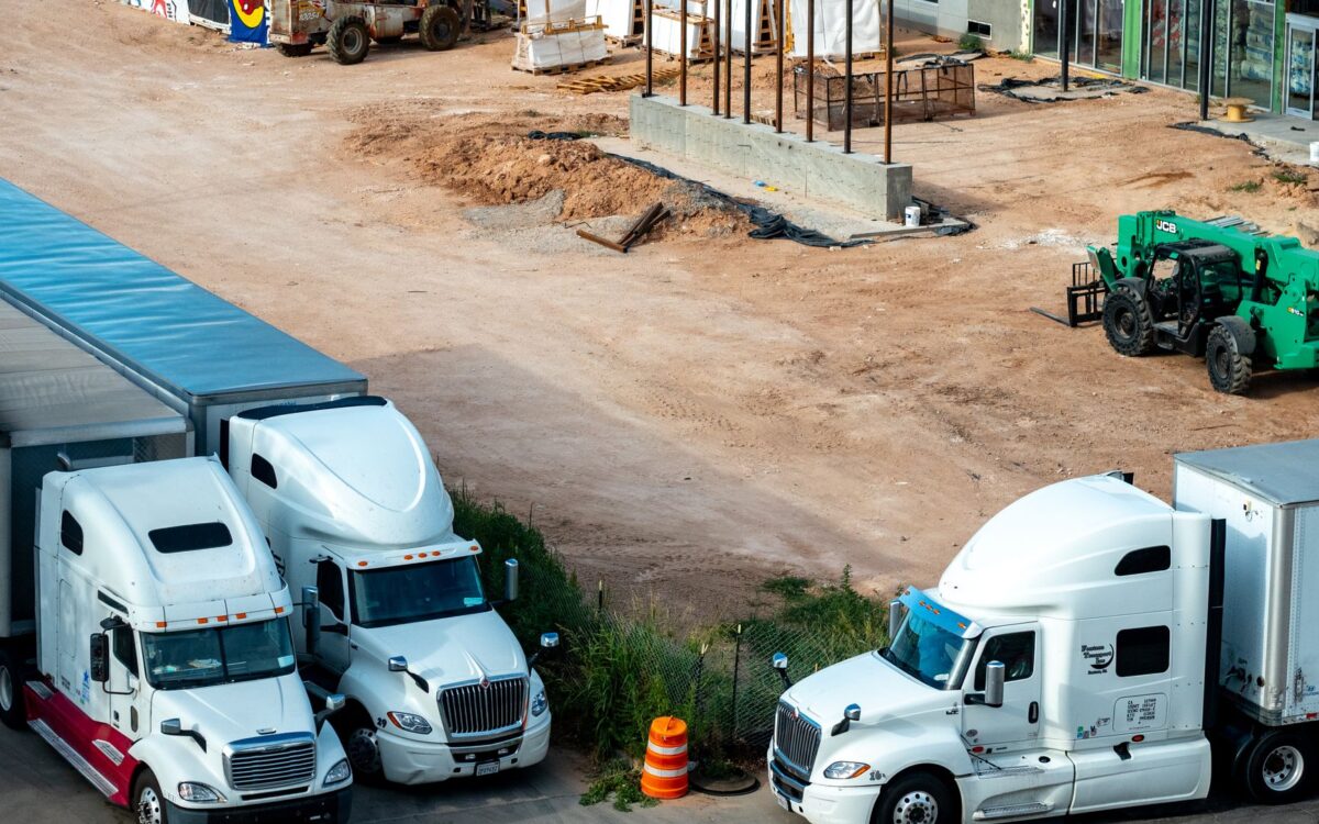 Construction equipment rental process in Utah showing delivery truck with cranes and forklifts arriving at job site