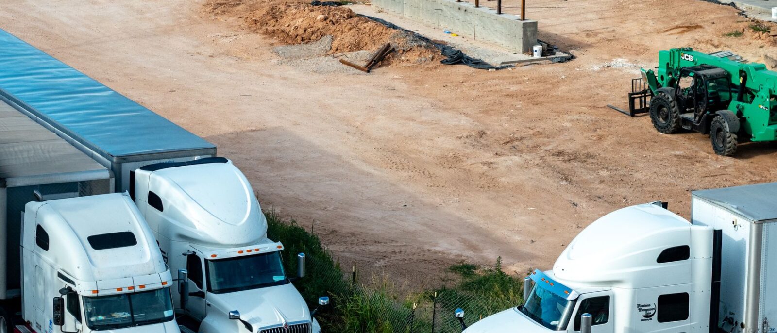 Construction equipment rental process in Utah showing delivery truck with cranes and forklifts arriving at job site
