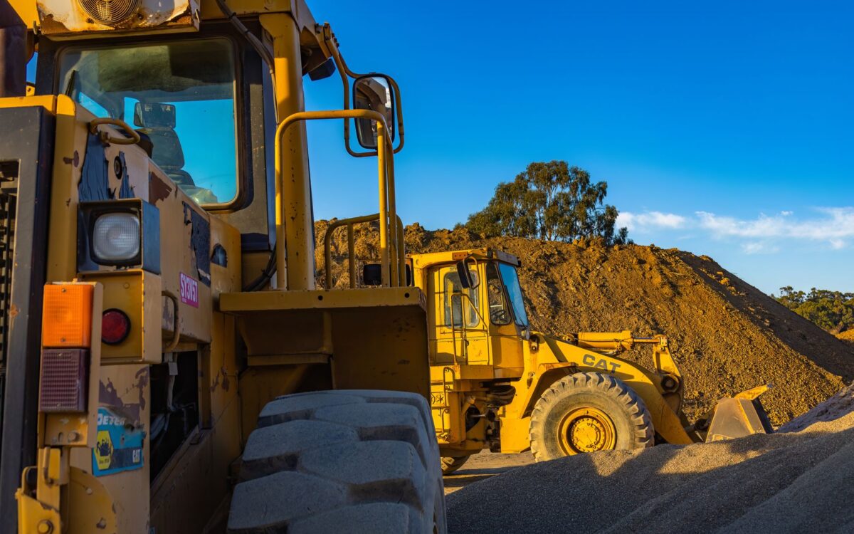 Industrial machinery operating outdoors, showcasing a bulldozer and a loader amidst piles of soil.