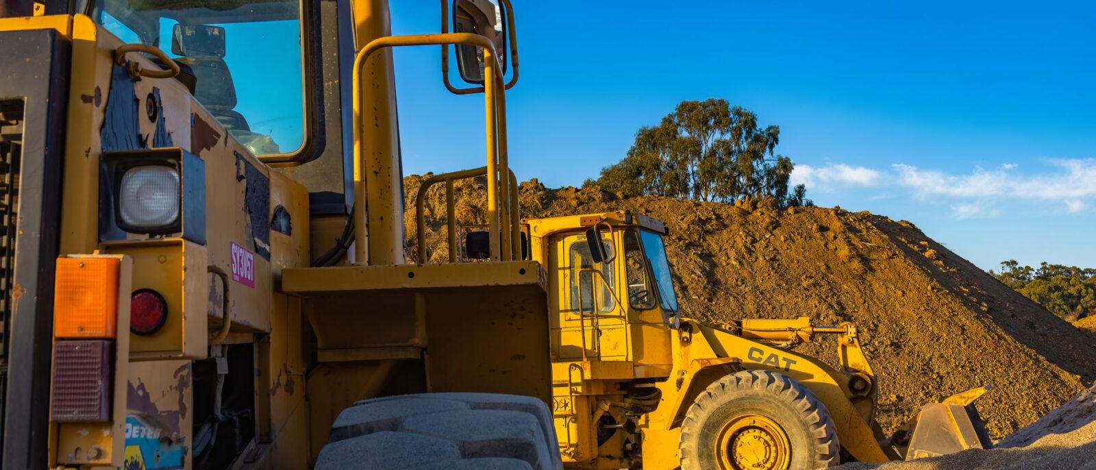 Industrial machinery operating outdoors, showcasing a bulldozer and a loader amidst piles of soil.