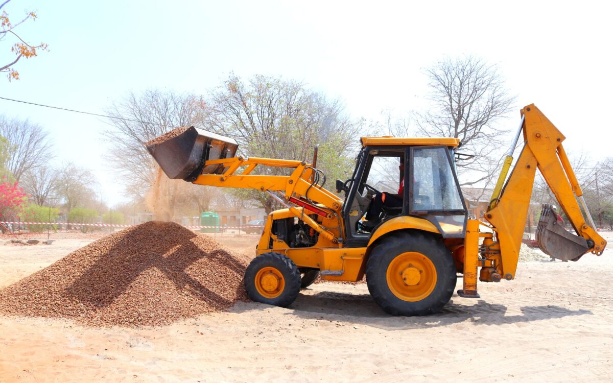 A yellow excavator moving gravel at an outdoor construction site during the day with clear skies.
