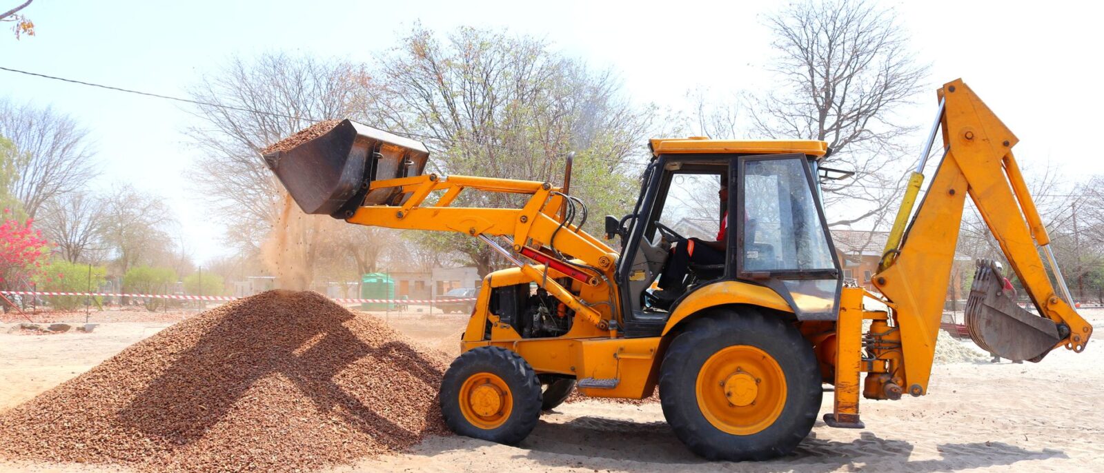 A yellow excavator moving gravel at an outdoor construction site during the day with clear skies.