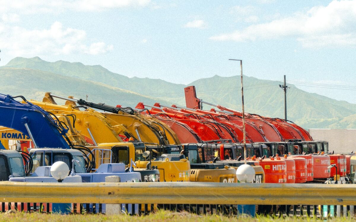 A lineup of vibrant construction vehicles against a beautiful mountain backdrop.