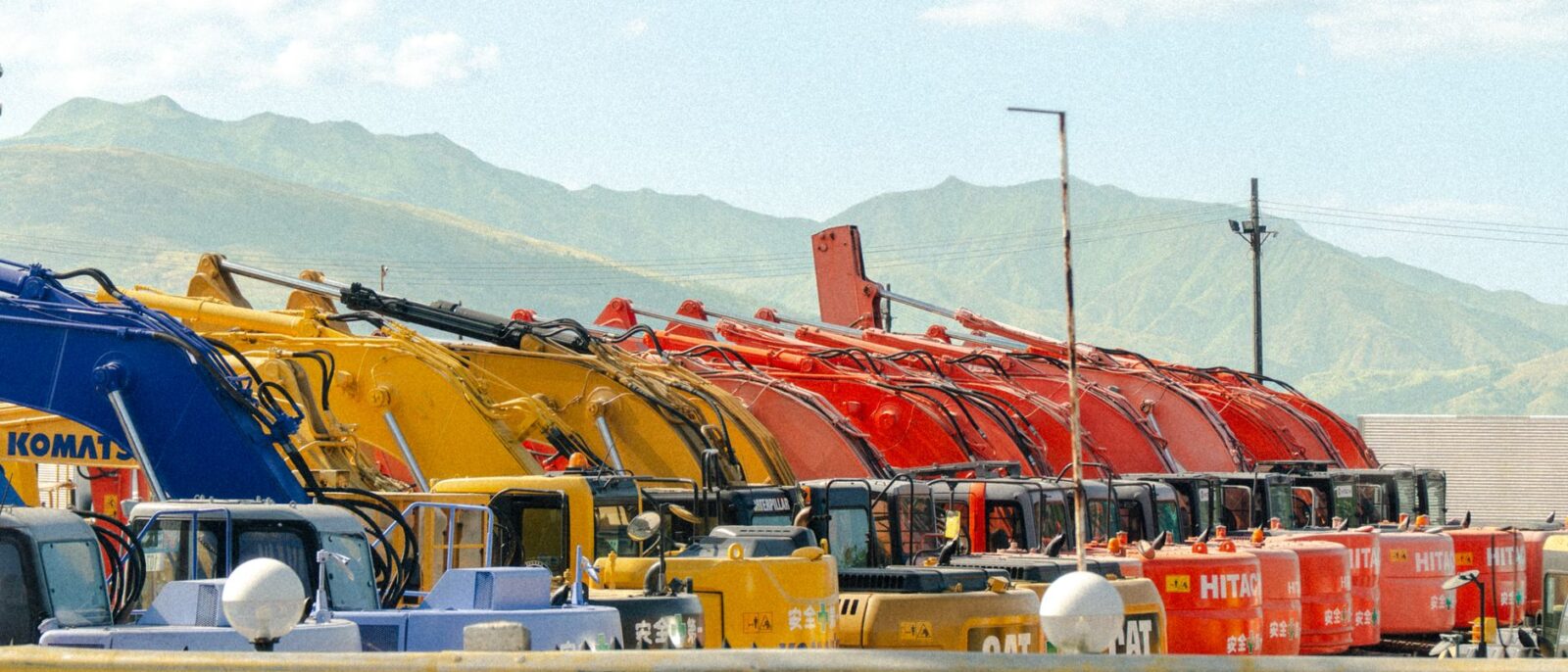 A lineup of vibrant construction vehicles against a beautiful mountain backdrop.