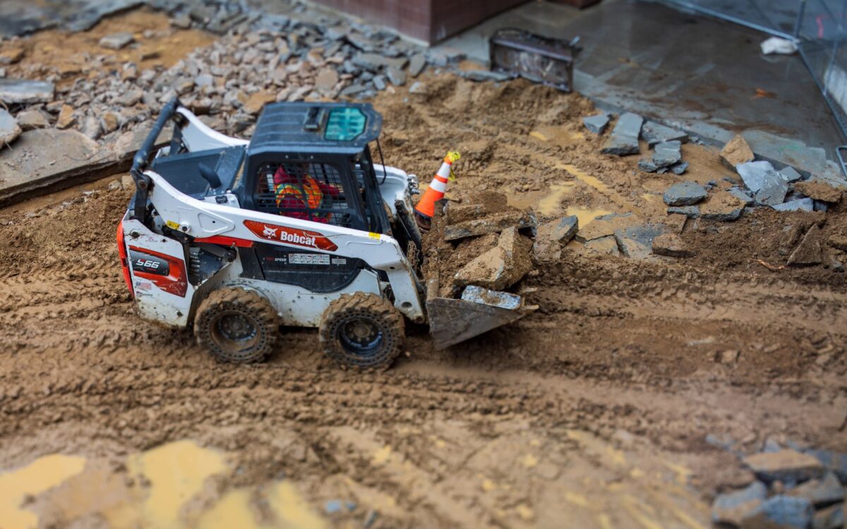 A skid steer loader moves rocks on a muddy construction site, showcasing construction machinery in action.