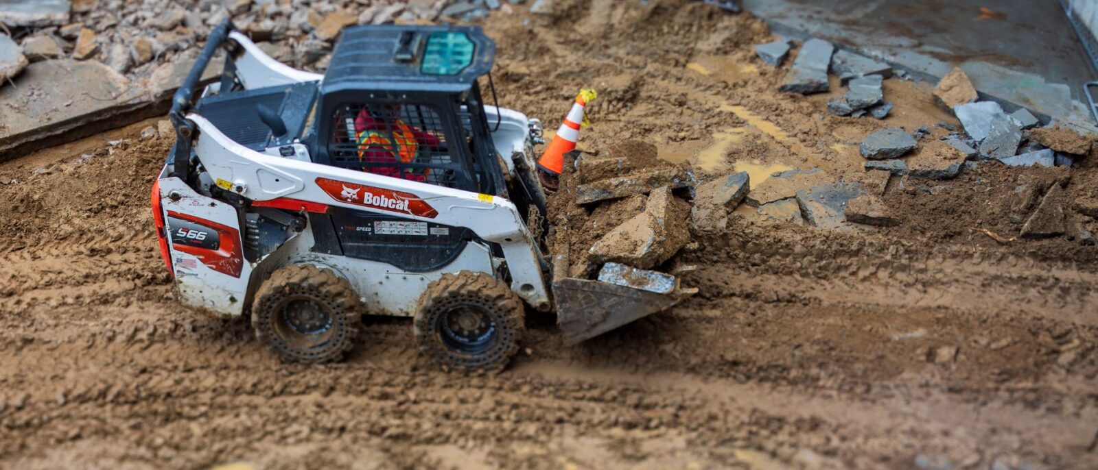 A skid steer loader moves rocks on a muddy construction site, showcasing construction machinery in action.