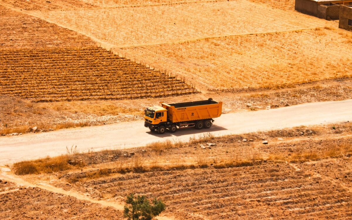 Aerial view of an orange dump truck on a rural road surrounded by dry fields and agricultural land.