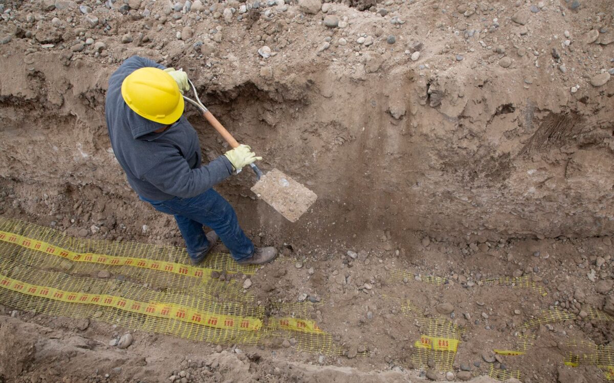 Overhead view of a construction worker digging a trench using a shovel at a site.
