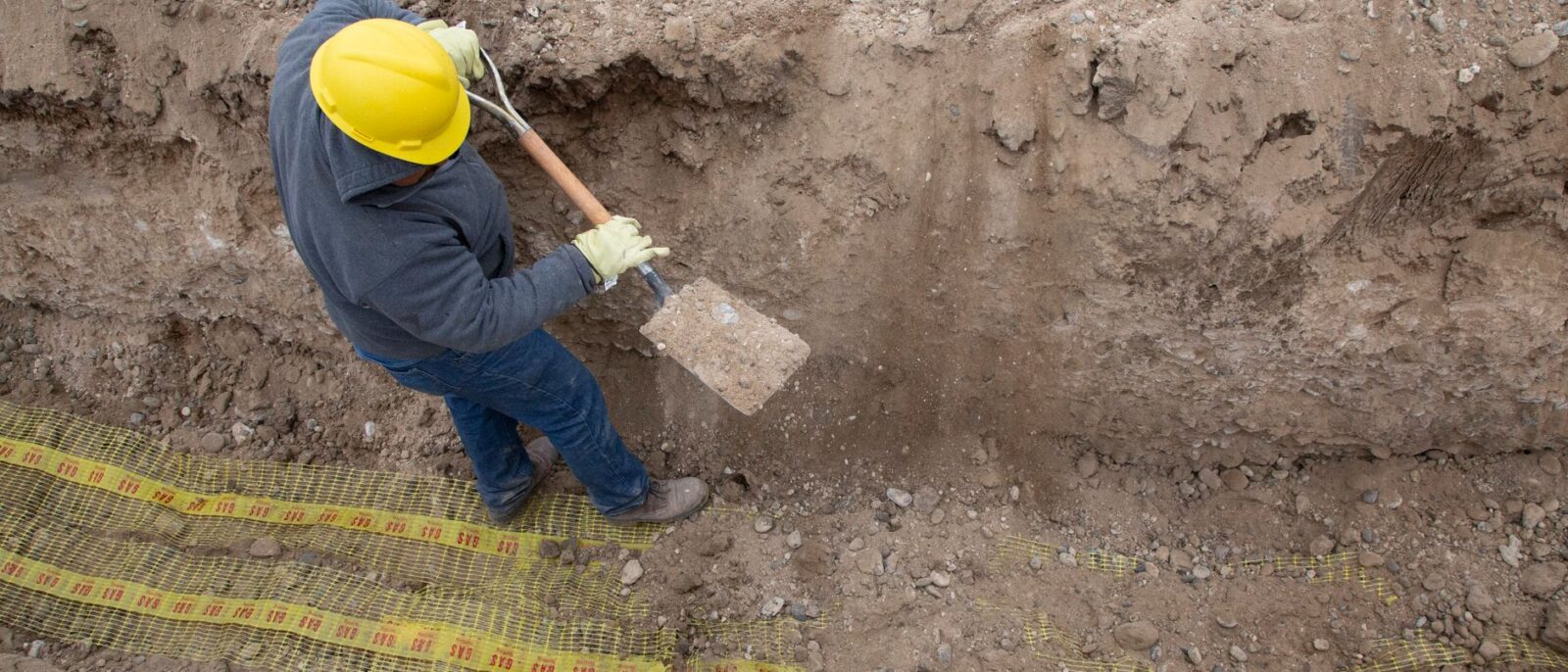 Overhead view of a construction worker digging a trench using a shovel at a site.