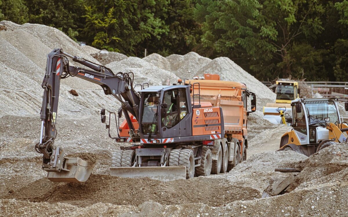 Excavator and machinery at a bustling construction site with piles of sand.