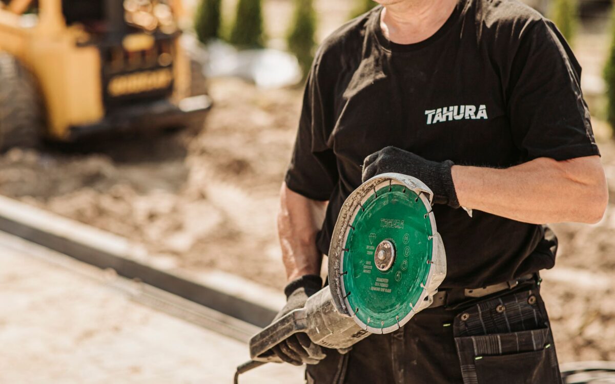 Male construction worker in protective gear using a circular saw outdoors on a sunny day.