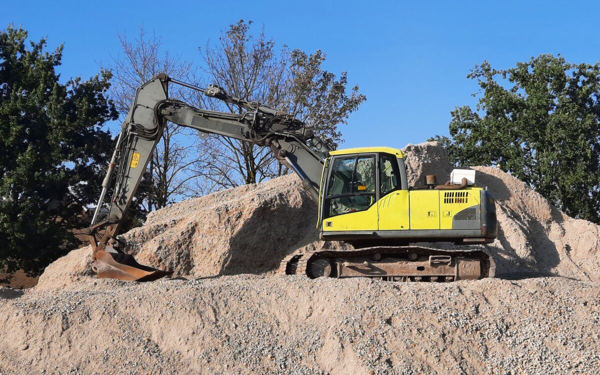 A yellow excavator working on a gravel mound at a construction site.