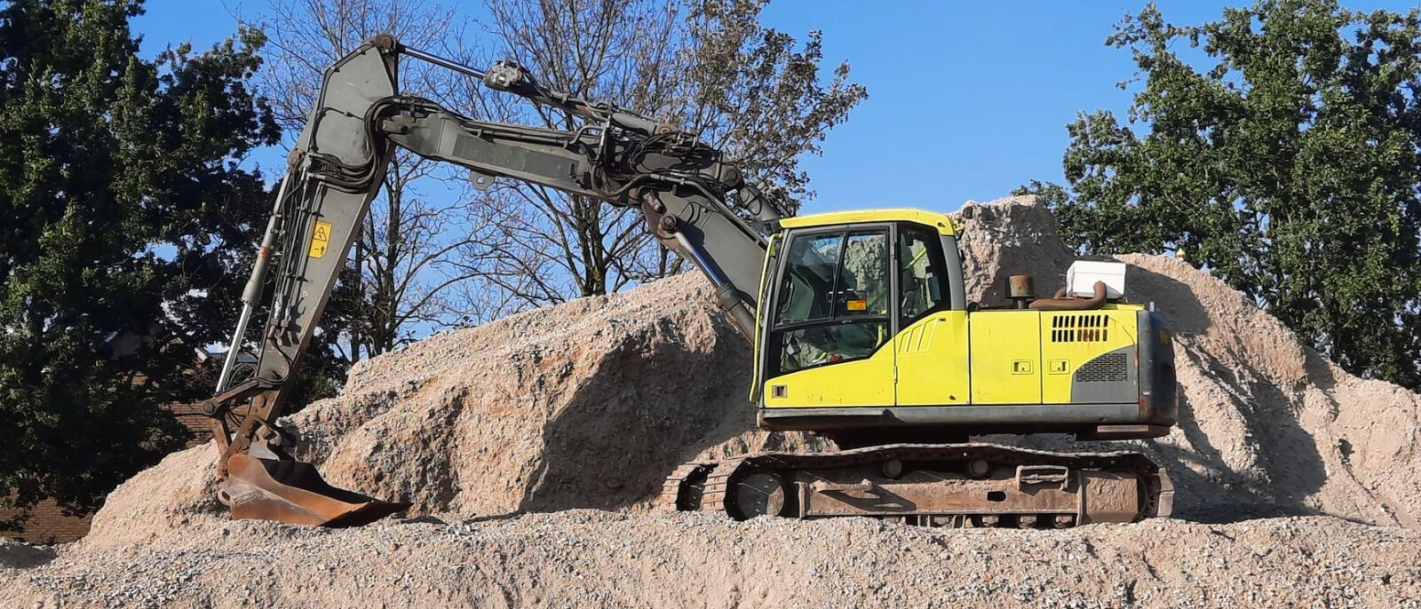 A yellow excavator working on a gravel mound at a construction site.