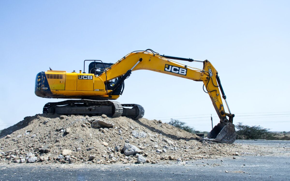 Yellow excavator on a pile of dirt at a construction site under clear blue sky.