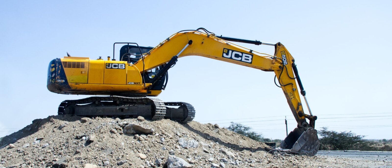 Yellow excavator on a pile of dirt at a construction site under clear blue sky.