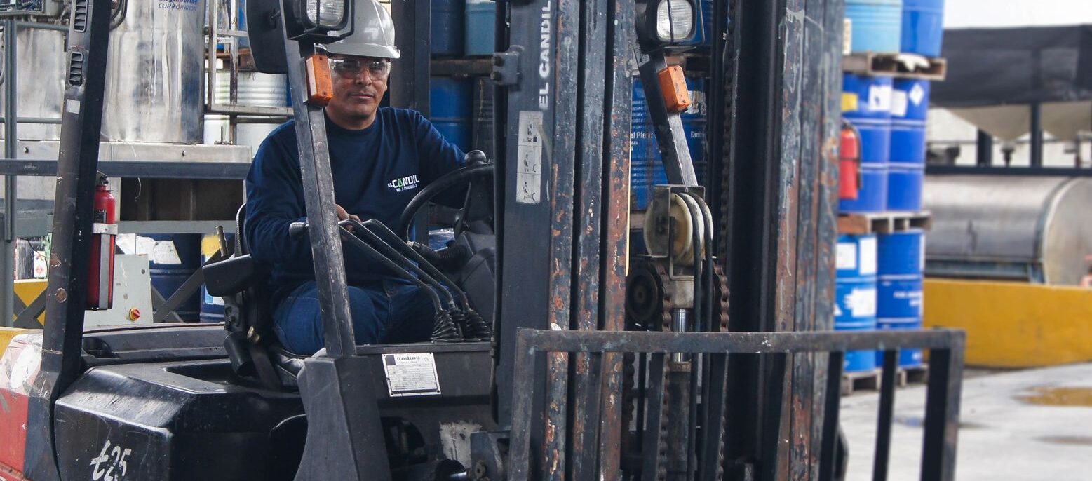 Warehouse scene with worker operating a forklift among blue barrels.