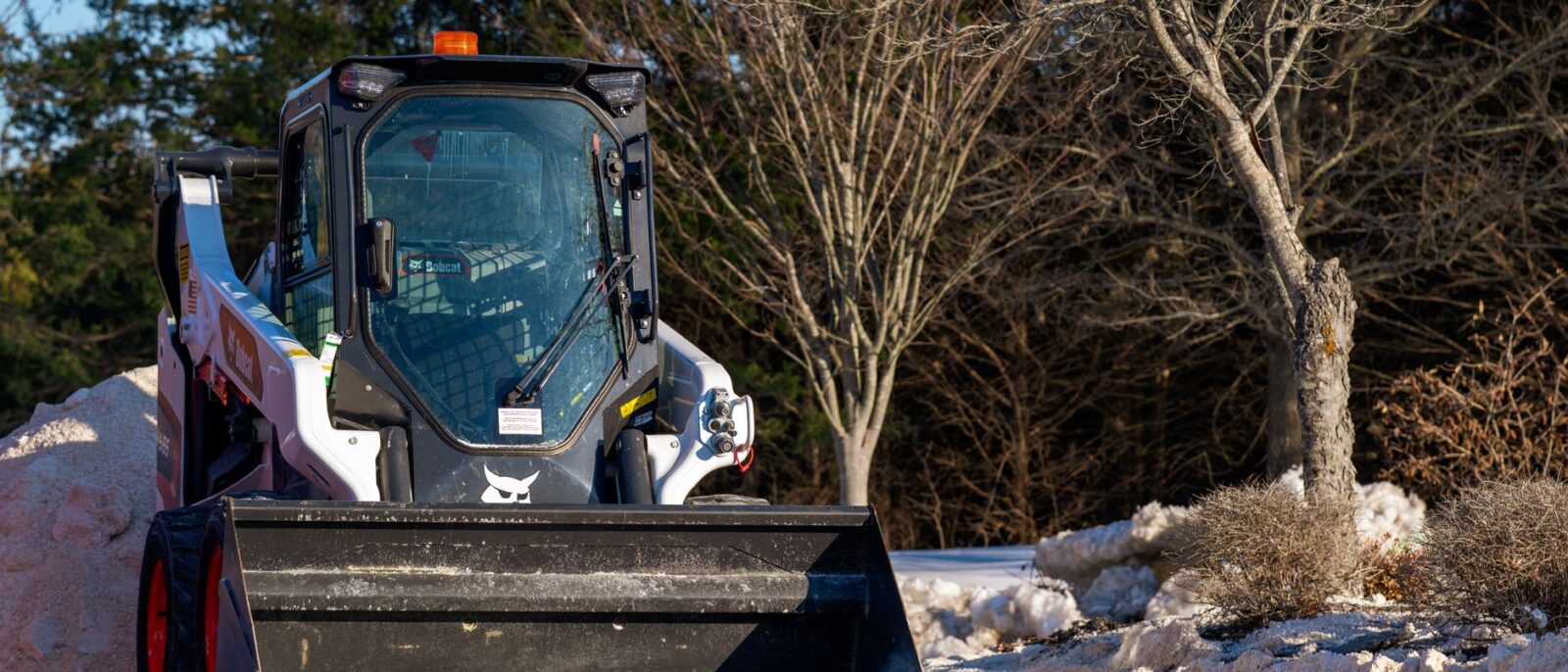 A skid steer loader clearing snow on a bright winter day outdoors in Virginia, USA.